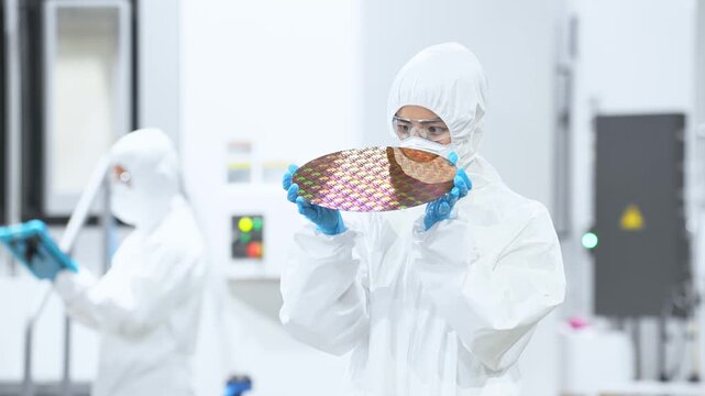 半導体工場でシリコンウエハーを検査する防護服を着た女性作業員