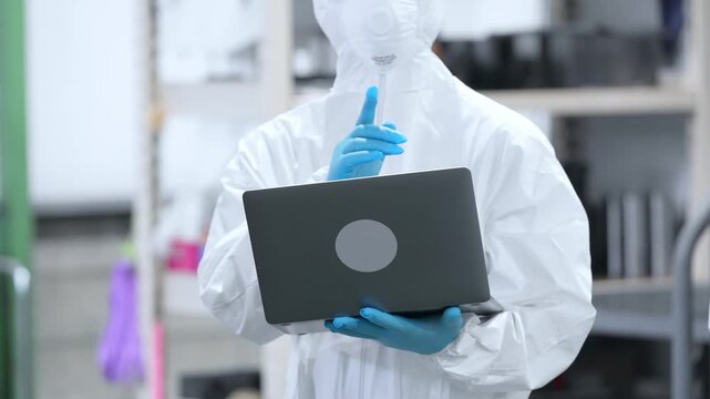 ノートパソコンを持って工場で作業する防護服を着た男性作業員