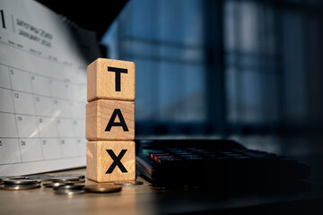 Wooden blocks spelling TAX with coins, calculator and calendar on desk. Symbolizing tax payment, deadline, financial planning and accounting concept.