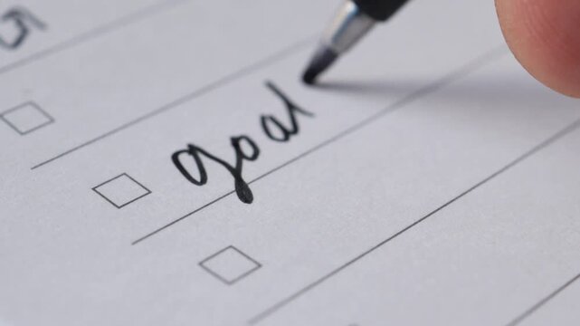 Close up of person writing goals plan and action on checklist with black pen and marking with red ink