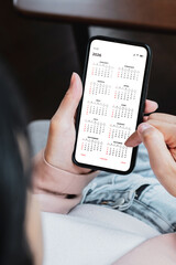 Young woman using smartphone with monthly calendar to plan 2026 activities. Scheduling and organizing plans. Technology and business concept.