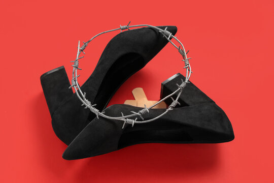 High-heeled shoes with plasters and barbed wire on red background. Uncomfortable shoes concept