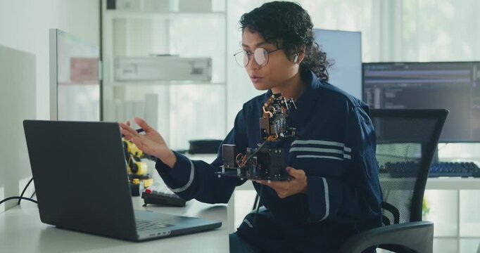 Young African American female robotics engineer discussing mechanical part on video call in laboratory. Remote work, virtual training, online meeting, future technology, technical support concept.
