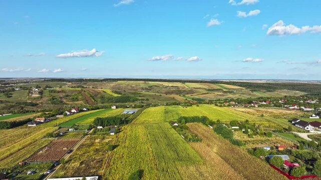 Agricultural field between Romanian houses, clouds passing by on a splendid sunny day - aerial of Botosani