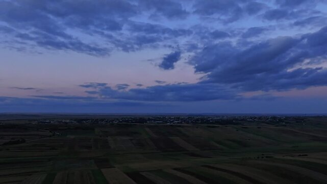Blue hour aerial hyper lapse, flyover Romanian hills, drifting clouds over Botosani agricultural landscape