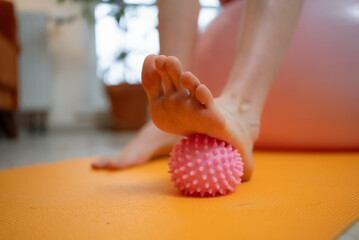 Pregnant woman strengthening her feet and relieving discomfort by rolling a spiky massage ball on a...