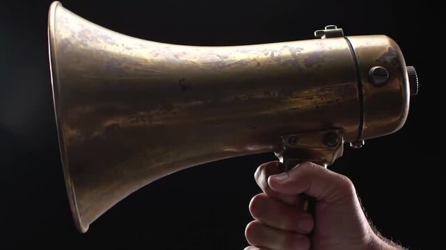 A close-up shot of a hand holding a vintage brass megaphone against a dark background, highlighting the tool's texture. The aged megaphone is centered