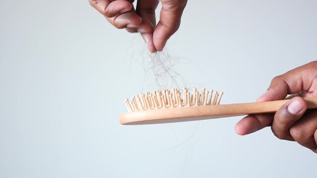 Person removing fallen hair from wooden comb on white background showing hair loss problem