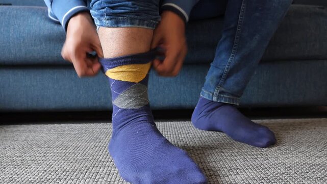 Man on a sofa pulls up his jeans to reveal argyle socks and then lowers his jeans, showcasing the dynamic motion and changing fashion style