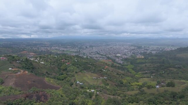 A panoramic aerial capture of the lush hills surrounding Popay&aacute;n under a cloudy sky, showcasing the city's buildings in the distance.