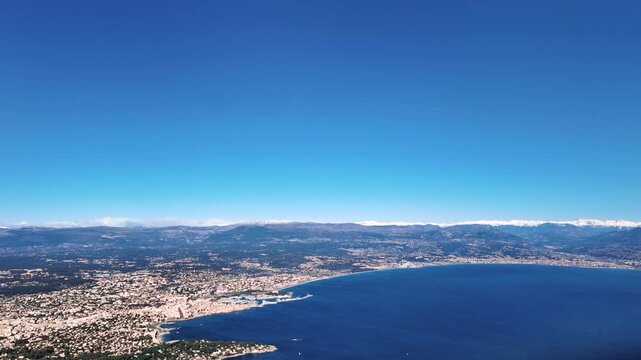 Elevated aerial view of french Antibes city in C&ocirc;te d&rsquo;Azur captured from an airplane cockpit in the approach to Nice aiport (NCE) in a splendidi winter morning with the snow-capped Alps as background