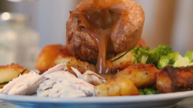 Slow-motion gravy pour over a fluffy, hollow Yorkshire pudding with Roast dinner including chicken, potatoes, veg. Ideal for culinary tutorials, comfort food montages, and restaurant social media ads.