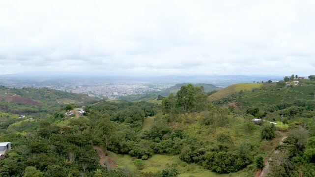 Aerial view of lush green hills under a cloudy sky, overlooking the city of Popay&aacute;n in Colombia.