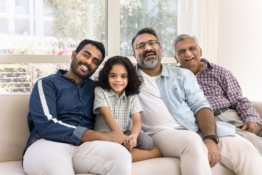 Four generations of family sit together on couch, older male, younger man, and child, smiling, posing for photo at home, radiates warmth, connection and bond between family members of different ages