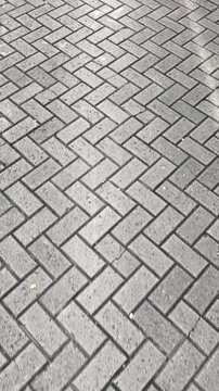 A rhythmic arrangement of herringbone paving blocks. Gliding over interlocking, weathered gray basalt paving. Vertical shot, moving forward. 4k 60 fps.