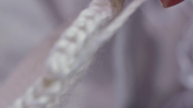 Close-up of white yarn being knitted into a textured pattern, showcasing the intricate details of the stitches and the soft fibers against a blurred background