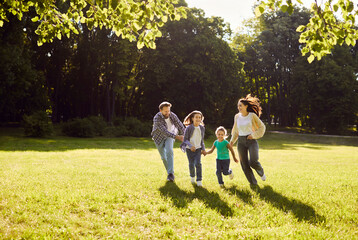 Fototapeta premium Happy friendly family enjoy running together, moving in green field, park feeling connection and enjoying peaceful day, warm sunny light, summer fun weekend to enjoy beautiful nature day out