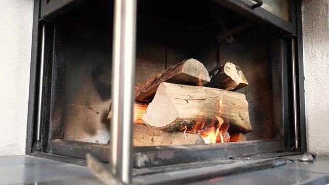 Slow motion view of a fireplace with burning logs and steady flames. The wider framing captures the warm ambient glow and the cozy atmosphere of a relaxing indoor setting.
