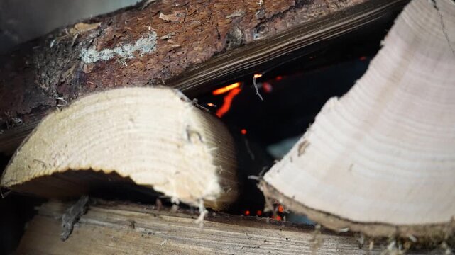 Close-up of faint glowing embers inside a fireplace with minimal smoke rising gently. The fire appears nearly out, capturing a quiet and subdued indoor moment.