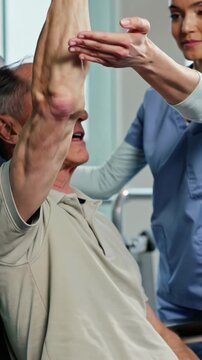 Senior male patient doing arm rehabilitation with physiotherapist, vertical footage