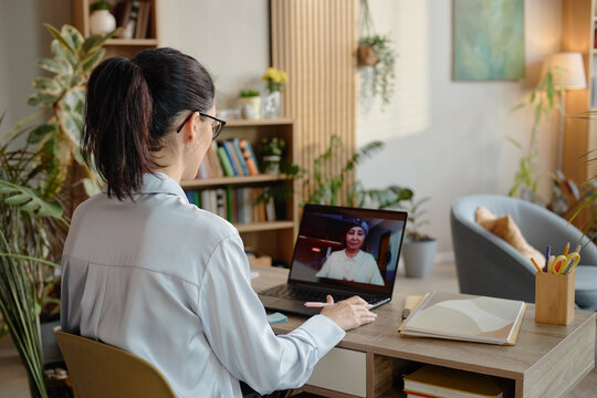 Caucasian young adult woman conducting online psychology session with Asian woman via laptop, sitting at desk in home office, engaging in virtual mental health consultation