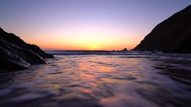 Golden sunset over calm ocean beach with rocky cliffs
