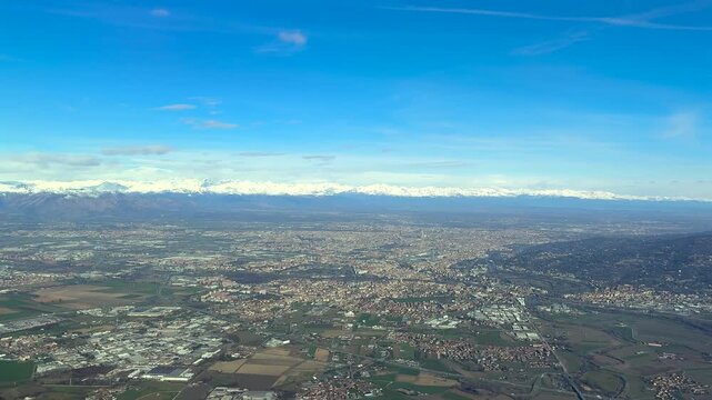 An aerial view of Turin city captured from an airplane cockpit, with a view of the city in the Po Valley, and the snowed Alps mountains in the background. Airplane cockpit view