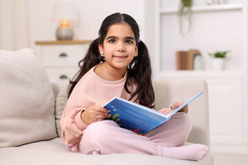 Fototapeta premium Cute little girl reading book on couch at home