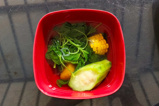 Indonesian clear vegetable soup or Sayur Bening with luffa, sweet corn, and spinach served in a red bowl.