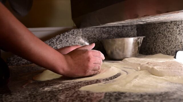 Pizza maker kneading dough with flour on a counter