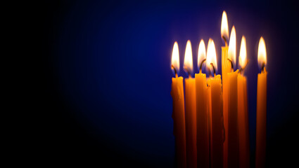 Fototapeta premium A cluster of tall yellow candles burning brightly against a dark blue background.