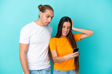 Fototapeta premium Young caucasian couple isolated on blue background reading a message with the mobile
