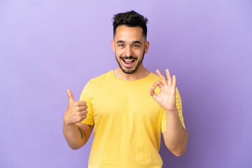 Fototapeta premium Young caucasian man isolated on purple background showing ok sign and thumb up gesture