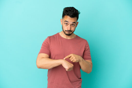 Young caucasian man isolated on blue background making the gesture of being late
