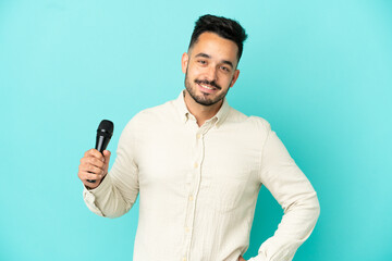 Naklejka premium Young caucasian singer man isolated on blue background posing with arms at hip and smiling