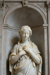 Fototapeta premium Marble Statue of a Serene Woman with Clasped Hands in an Ornate Niche, Classical Sculpture Style for Art or Historical Design Projects