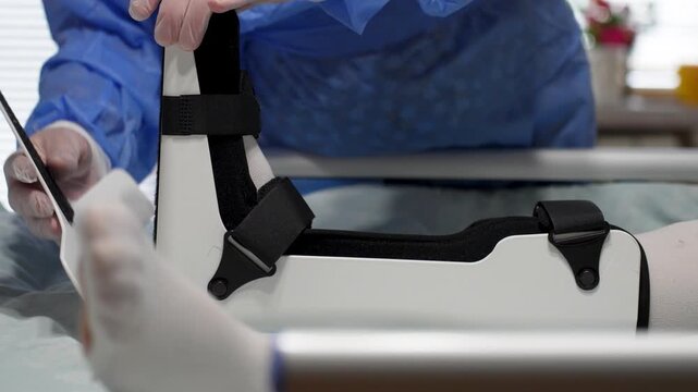Doctor Adjusting Patient Ankle Orthosis Brace. Close-up of a healthcare professional adjusting a white orthopedic boot on a patient leg. Focused medical care and rehabilitation.
