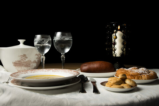 Mesa con sopa, embutido, galletas y dulce iluminada por vela.