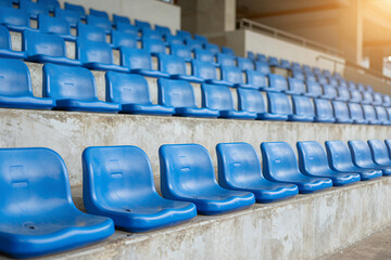 Fototapeta premium Rows of Empty Blue Plastic Stadium Seats in Tiered Stands with Warm Sunlight Glow on Concrete Steps and Bleachers for Sports Events or Concerts