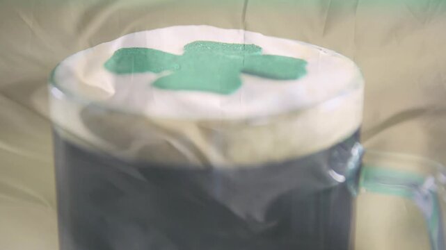 Camera pulling focus, clear glass mug revealing creamy foam and shamrock for product detail