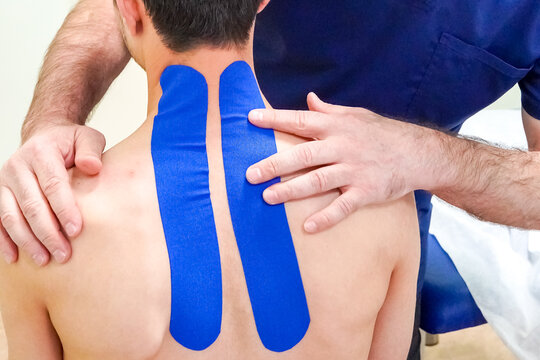 Physiotherapist treats patient neck, back pain with kinesio tape close up. Unrecognizable young caucasian patient.Doctor examining her patient back in medical office