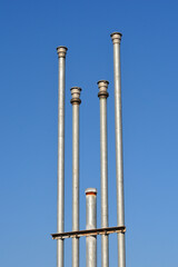 Four tall silver metal ventilation pipes and one shorter pipe are held together by a bracket against a clear blue sky