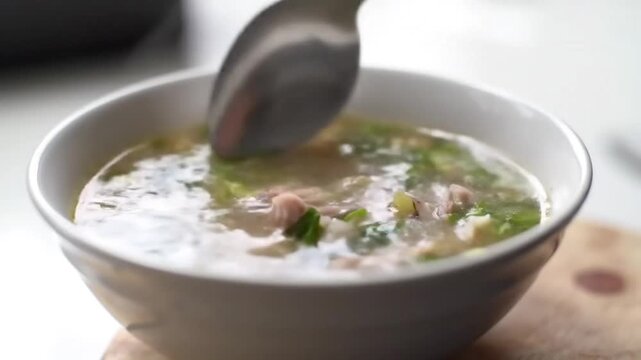 Close-up of spoon stirring warm chicken congee with green onions