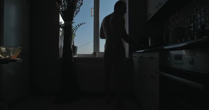 Silhouette of naked man making tea at the morning standing at window