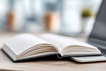 Obraz premium Close up of an open notebook with blank pages, next to a laptop on a wooden desk, creating a focused workspace environment suitable for creative work and study.