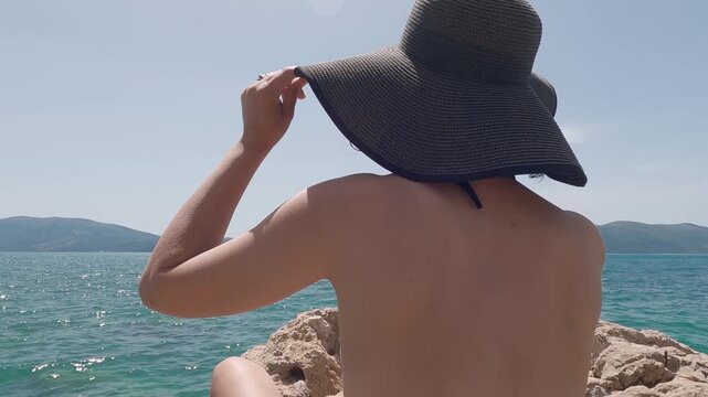 Woman in black hat enjoying seaside view during sunny summer vacation day