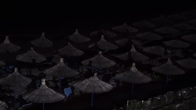 Beach with straw umbrellas illuminated by moon at night