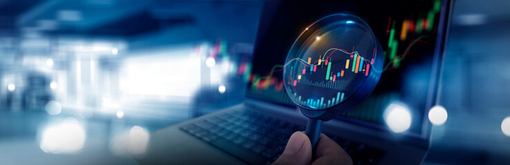 Magnifying glass over candlestick chart and digital financial diagram on laptop, Stock market data...