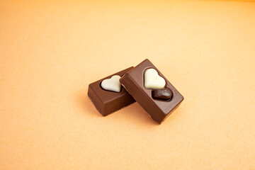 Two chocolate candy rectangles with hearts on cream background  and copy space, close up