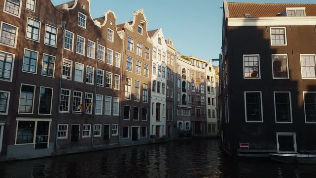 Iconic gabled canal houses along the Groenburgwal canal in Amsterdam illuminated by warm sunlight and reflecting in the water